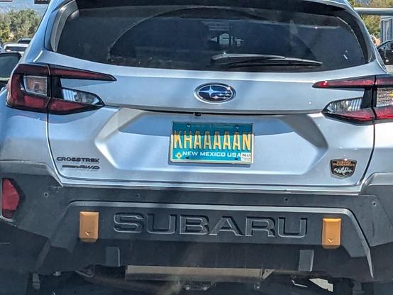 Photo of the rear of a Subara Crosstrek car, showing its teal blue New Mexico license plate. The plate ID is "KHAAAAAN".