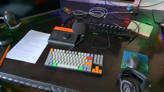 My music production desk into podcasting desk. There is a mic, audio interface, qwerty keyboard, mouse, headset, paper, pencil, and other objects not relevant for the podkast.