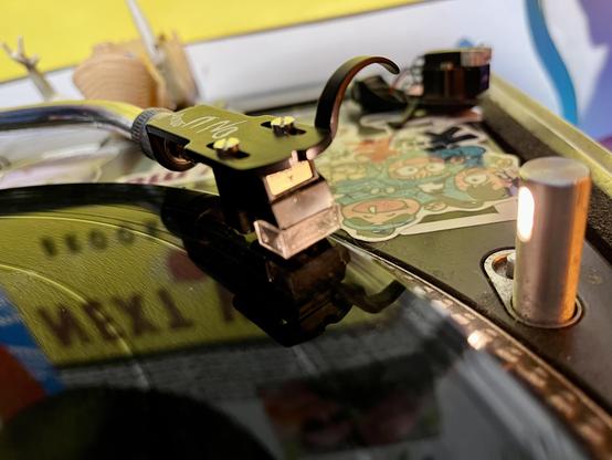 A close up of a stylus on a record, w bright light shines on the stylus and there's a spare cartridge and an ET toy in the background.
